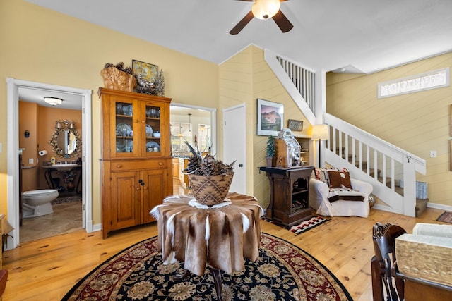 living room with light wood-type flooring, a ceiling fan, and stairs
