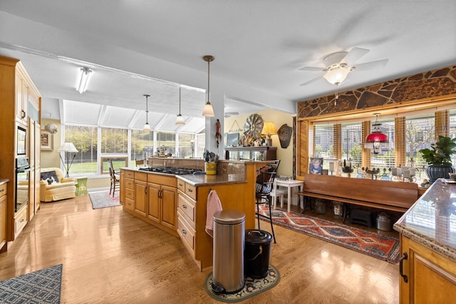kitchen featuring pendant lighting, ceiling fan, a kitchen bar, built in microwave, and light wood-style flooring