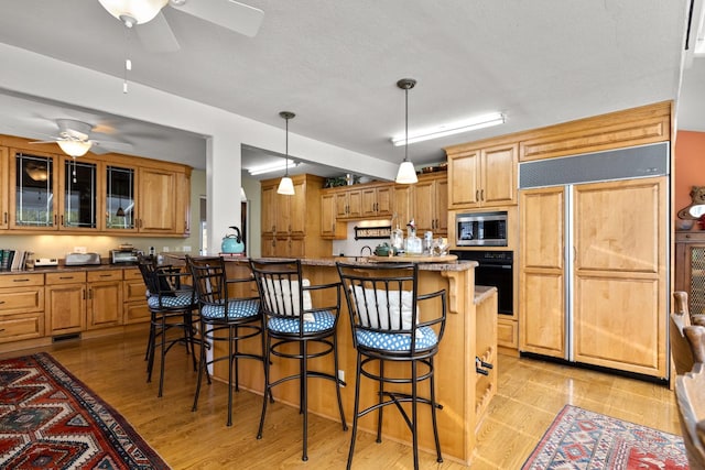 kitchen with a ceiling fan, built in appliances, a breakfast bar area, and glass insert cabinets