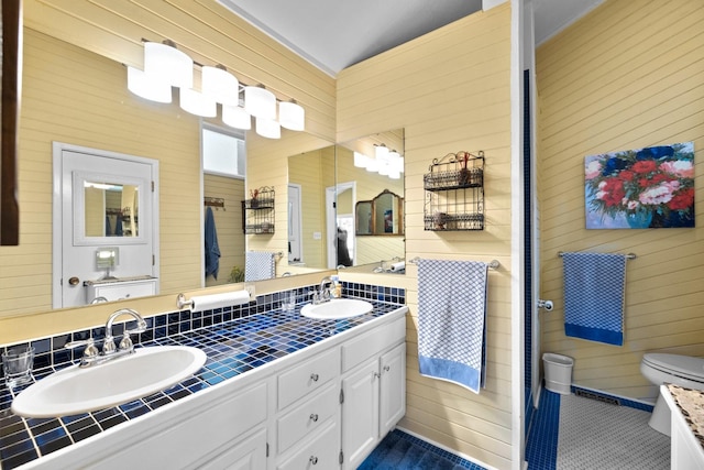 bathroom featuring double vanity, a sink, wooden walls, and toilet
