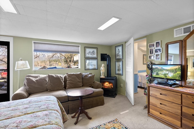 living area featuring light colored carpet, visible vents, a healthy amount of sunlight, and a wood stove