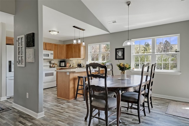 dining area with baseboards, visible vents, vaulted ceiling, and light wood-type flooring
