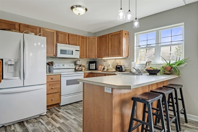 kitchen featuring white appliances, a peninsula, a sink, and light wood-style floors