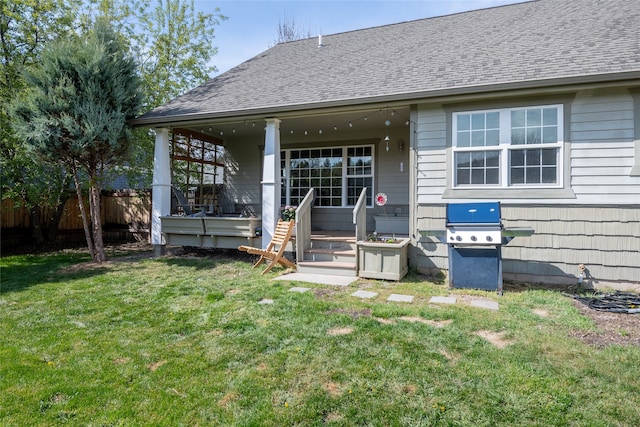 rear view of house featuring a lawn, fence, a shingled roof, and covered porch