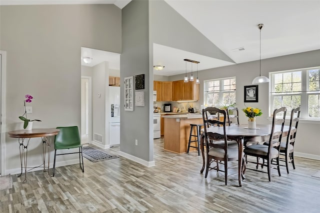 dining space with light wood-style floors, high vaulted ceiling, baseboards, and visible vents