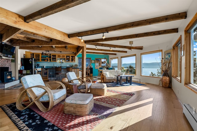 living area with a fireplace, beamed ceiling, hardwood / wood-style floors, and a baseboard radiator