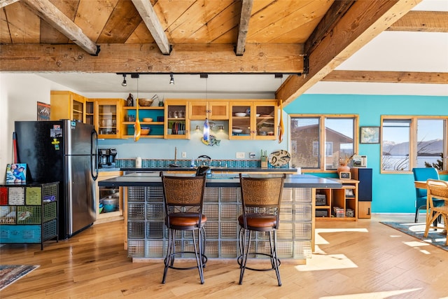kitchen featuring freestanding refrigerator, beam ceiling, light wood-style flooring, and a center island