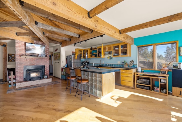 kitchen with beam ceiling, dark countertops, light wood-style floors, a kitchen bar, and stainless steel appliances