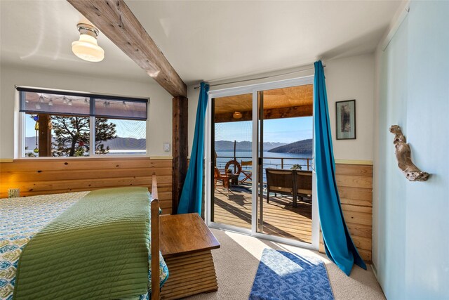 bedroom featuring beam ceiling, access to exterior, wooden walls, a water view, and carpet