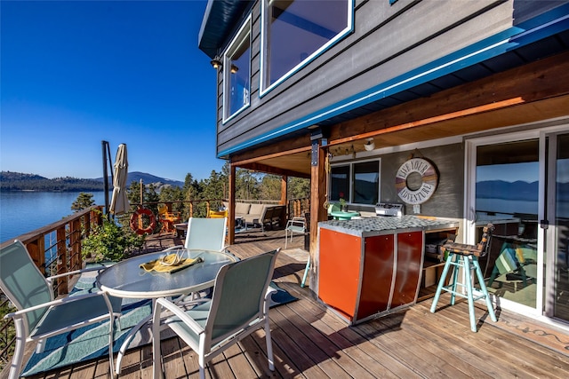 wooden deck with a water and mountain view, outdoor dry bar, and outdoor dining space