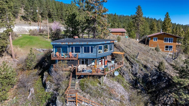 rear view of property with stairs, a deck, and a wooded view