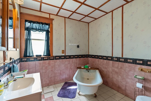 bathroom featuring a freestanding bath, vanity, tile patterned floors, wallpapered walls, and tile walls