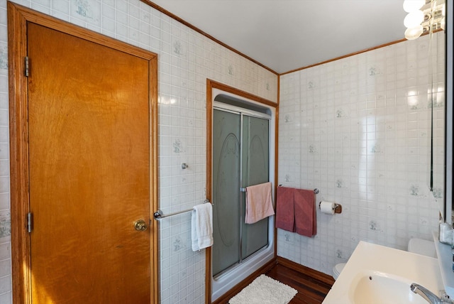 full bath with wood finished floors, ornamental molding, a sink, and a stall shower