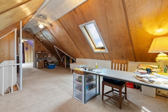 carpeted office space with wood walls, a ceiling fan, and vaulted ceiling with skylight