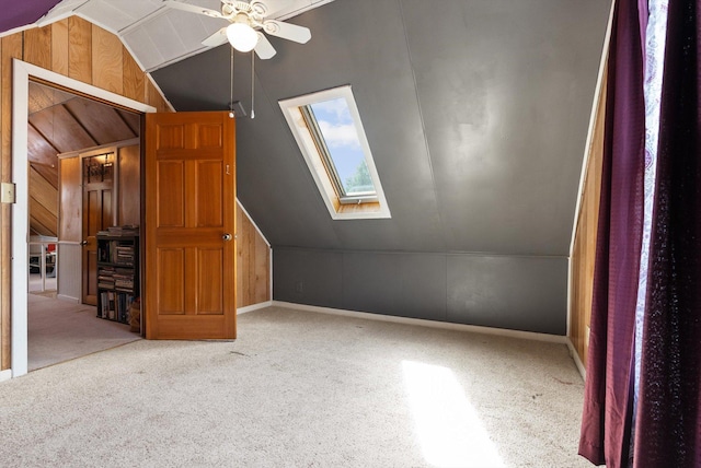 bonus room featuring vaulted ceiling with skylight, carpet floors, ceiling fan, and wooden walls