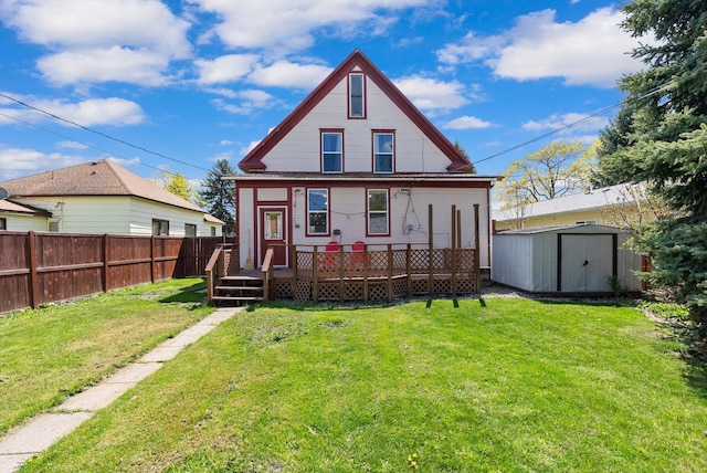rear view of house featuring fence, a wooden deck, a shed, an outbuilding, and a lawn