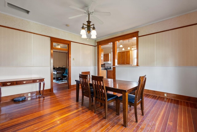 dining room with wainscoting, a ceiling fan, baseboards, visible vents, and hardwood / wood-style flooring