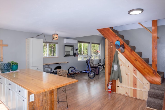 interior space with wood finished floors, wooden counters, open floor plan, an AC wall unit, and white cabinetry