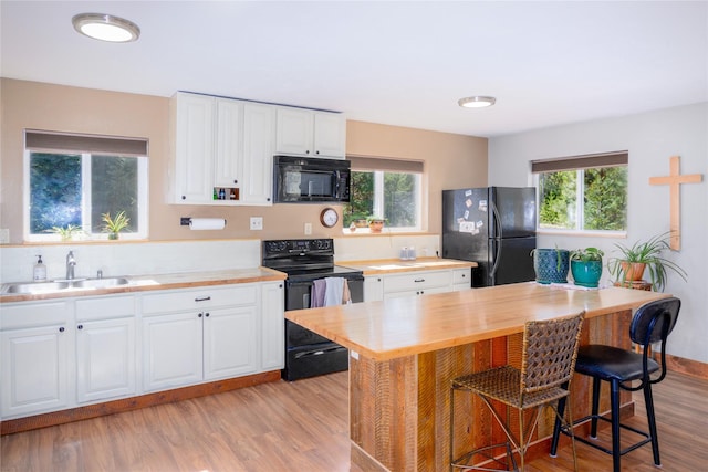 kitchen with light wood-style flooring, a breakfast bar area, black appliances, and white cabinetry