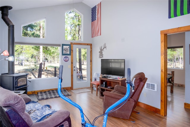 living area featuring visible vents, a wood stove, wood finished floors, and high vaulted ceiling