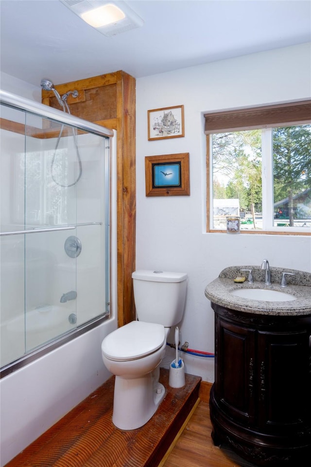full bathroom with vanity, bath / shower combo with glass door, wood finished floors, and toilet
