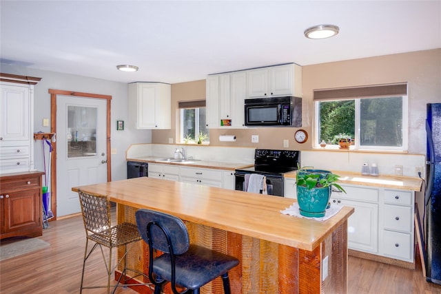 kitchen with plenty of natural light, white cabinets, black appliances, and light wood-type flooring