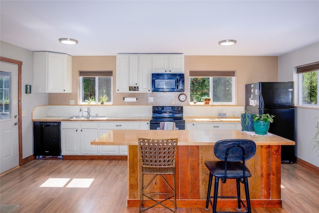 kitchen featuring white cabinetry, a sink, black appliances, a breakfast bar, and light wood-style flooring