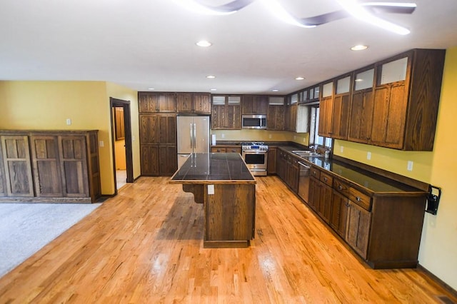 kitchen featuring dark brown cabinetry, dark countertops, light wood-type flooring, a sink, and stainless steel appliances