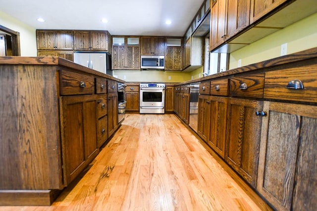 kitchen with appliances with stainless steel finishes, dark brown cabinets, light wood finished floors, glass insert cabinets, and recessed lighting