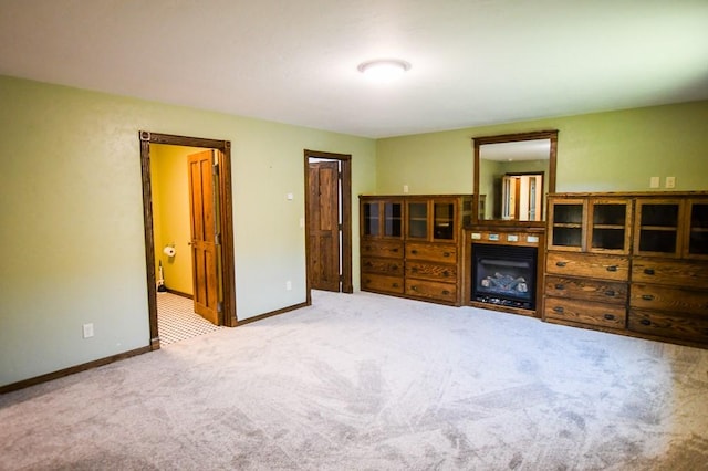 interior space featuring baseboards, a glass covered fireplace, and carpet