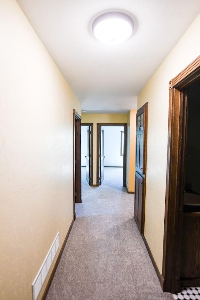 corridor with baseboards, visible vents, and light carpet