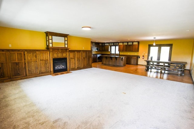 unfurnished living room featuring a fireplace with flush hearth, carpet, wood finished floors, and a healthy amount of sunlight