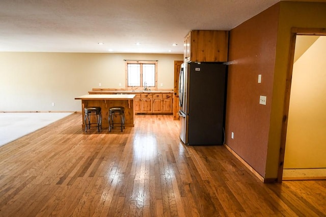 kitchen featuring freestanding refrigerator, a kitchen island, a kitchen breakfast bar, light countertops, and light wood finished floors