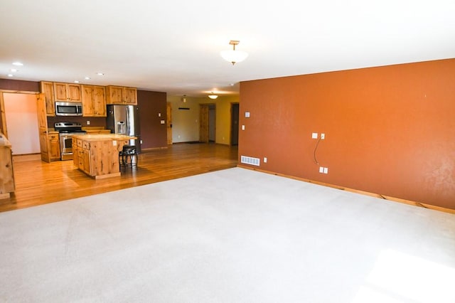 kitchen featuring a kitchen island, baseboards, open floor plan, light colored carpet, and appliances with stainless steel finishes
