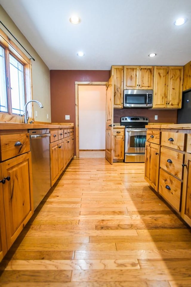 kitchen with brown cabinetry, a sink, light wood finished floors, stainless steel appliances, and recessed lighting