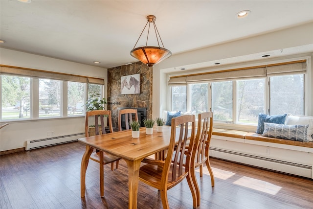 dining room featuring wood finished floors, baseboard heating, a stone fireplace, and a wealth of natural light