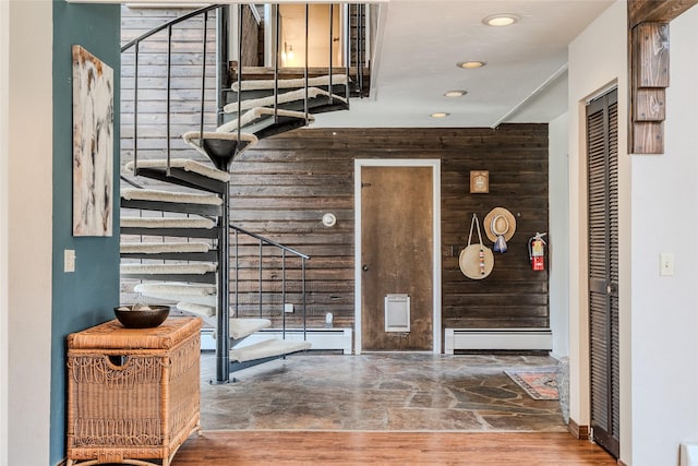 foyer entrance with wood walls, stairs, baseboard heating, recessed lighting, and stone finish flooring