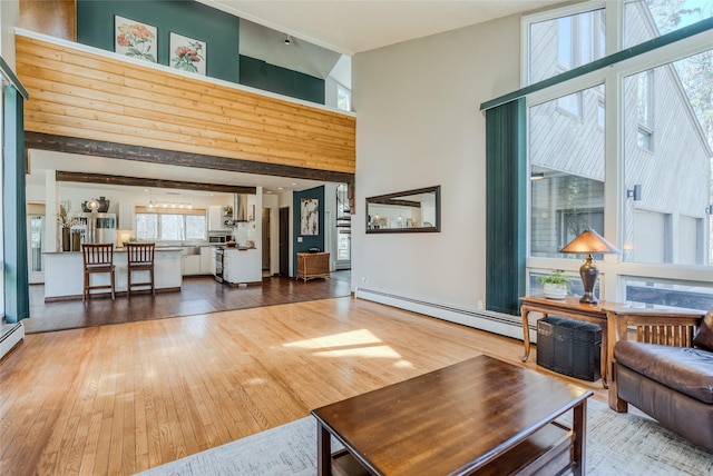 living area with a high ceiling, baseboard heating, and hardwood / wood-style flooring