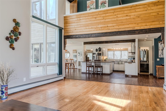 living room featuring wood-type flooring, a high ceiling, and baseboard heating