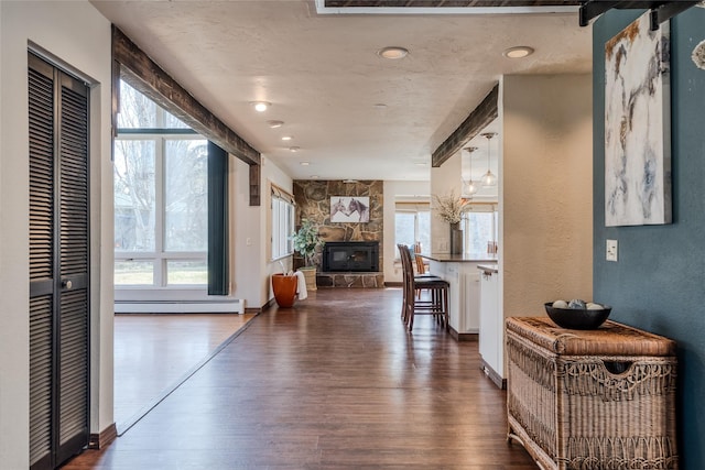 hall featuring a textured wall, a baseboard heating unit, a healthy amount of sunlight, and dark wood finished floors