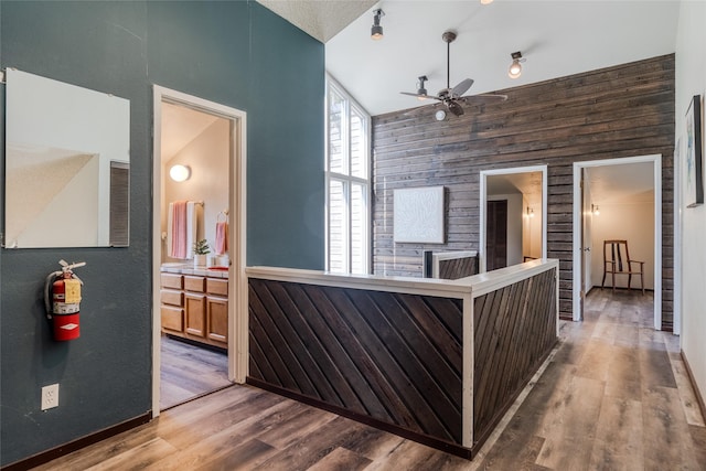 hall featuring wood walls, wood finished floors, and high vaulted ceiling