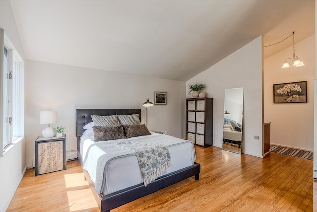 bedroom with lofted ceiling, baseboards, a baseboard heating unit, light wood finished floors, and a notable chandelier