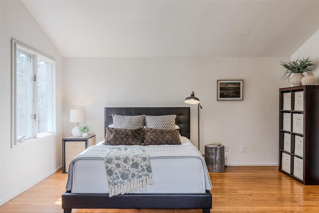 bedroom featuring baseboards, light wood-style flooring, and lofted ceiling