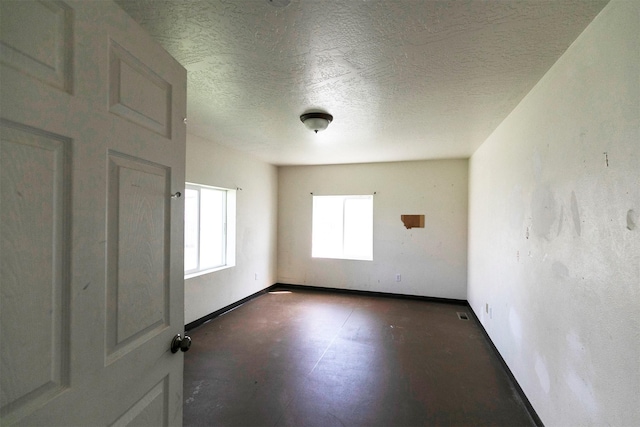 spare room with a textured ceiling, baseboards, and finished concrete floors