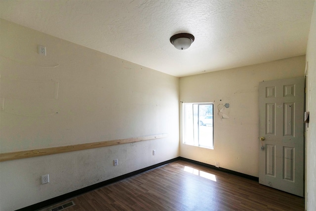unfurnished room featuring baseboards, dark wood-style floors, a textured ceiling, and visible vents