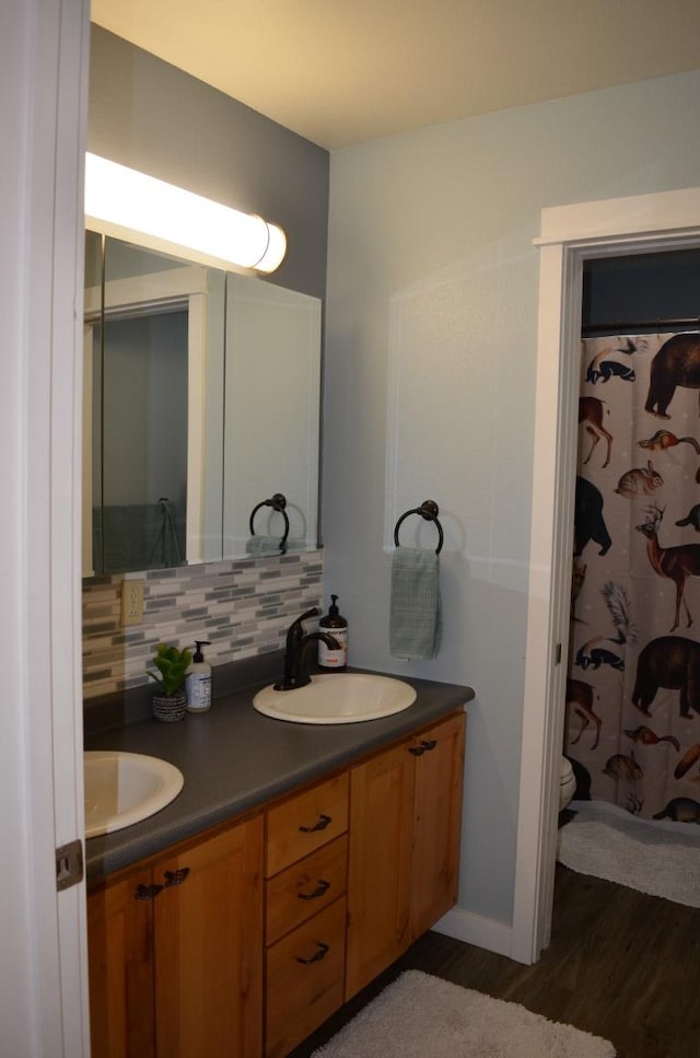 bathroom with double vanity, a sink, decorative backsplash, and wood finished floors