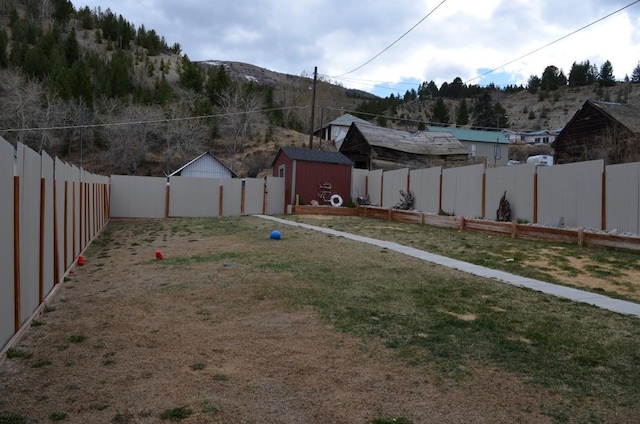view of yard featuring an outdoor structure, a fenced backyard, a mountain view, and a shed