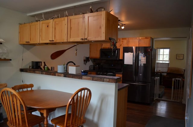 kitchen featuring range with gas stovetop, freestanding refrigerator, a peninsula, dark countertops, and dark wood finished floors