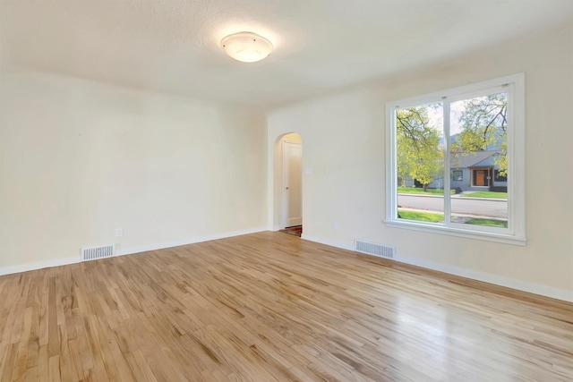 empty room featuring visible vents, arched walkways, baseboards, and light wood-type flooring
