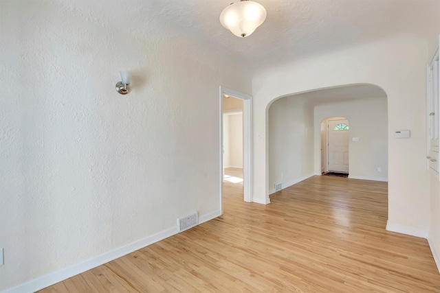 unfurnished room with visible vents, arched walkways, light wood finished floors, and baseboards